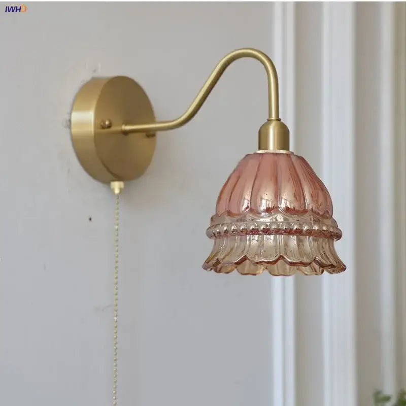 A delicate pink glass lampshade with a fluted design hangs from a brass arm in the decorbites led jellyfish wall lamp