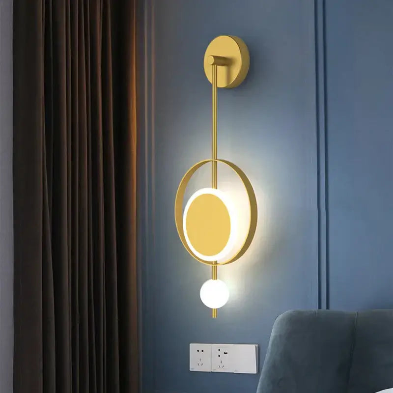 Gold-toned DecorBites™ LED Nordic wall light with circular ring, illuminated oval panel, and dangling spherical bulb for indoor decor