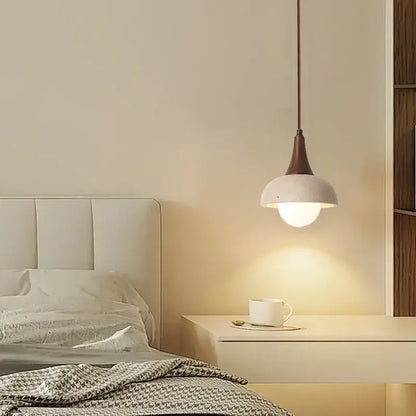 Modern decorbites led pendant lamp with matte white ceramic shade and dark bronze stem above bedside table