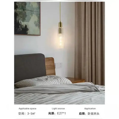Gold-toned decorbites led pendant light with cylindrical glass shade and exposed filament bulb hanging above bed