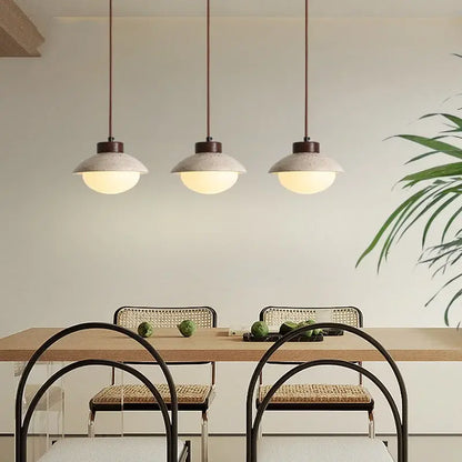 Three decorbites led pendant lights with yellow travertine wood and concrete shades hang above a dining table