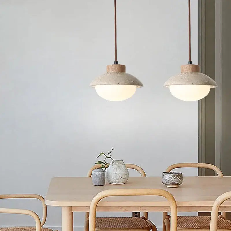 Two minimalist decorbites led pendant lights with matte beige ceramic and yellow travertine wood hang above a wooden table