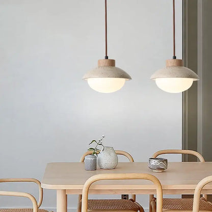 Two minimalist decorbites led pendant lights with matte beige ceramic and yellow travertine wood hang above a wooden table
