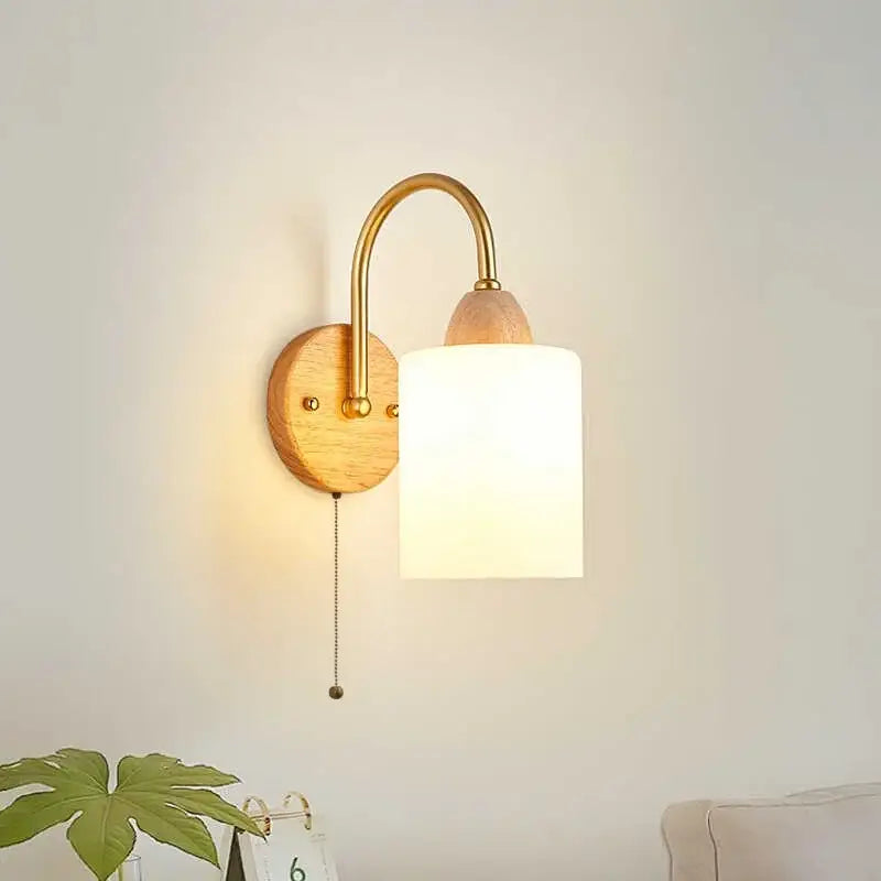 A warm-toned brass and wood decorbites led pull wall light with cylindrical frosted glass shade for bedroom decor