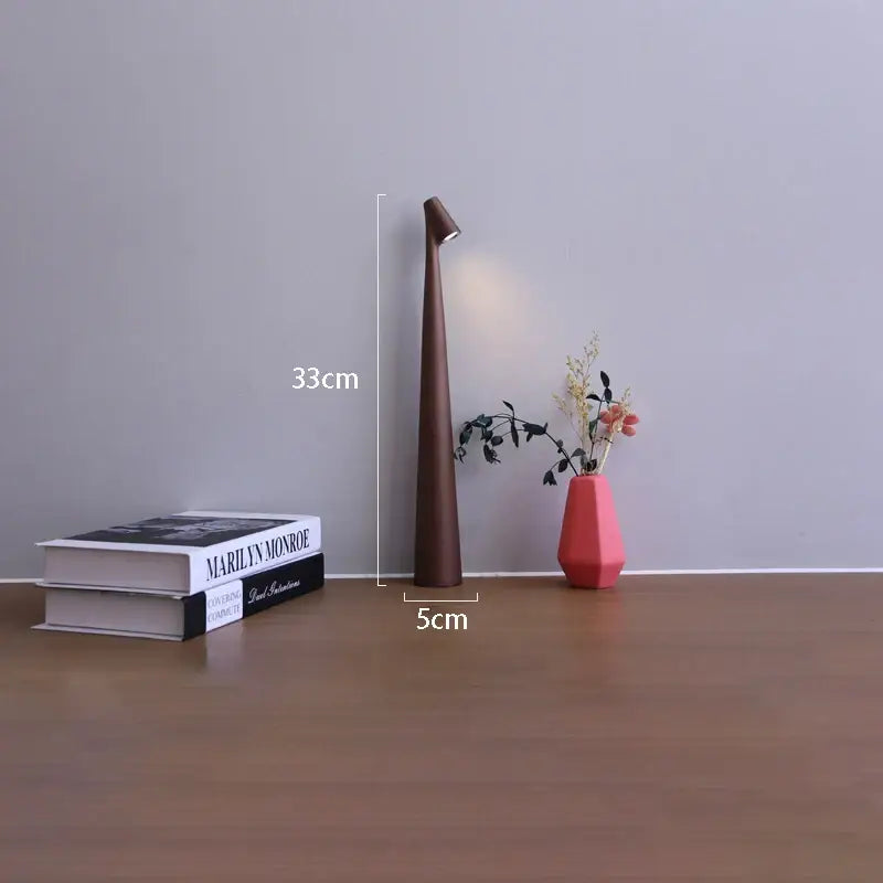 A sleek dark brown ceramic table lamp with tapered design and angled light fixture for led rechargeable desk use
