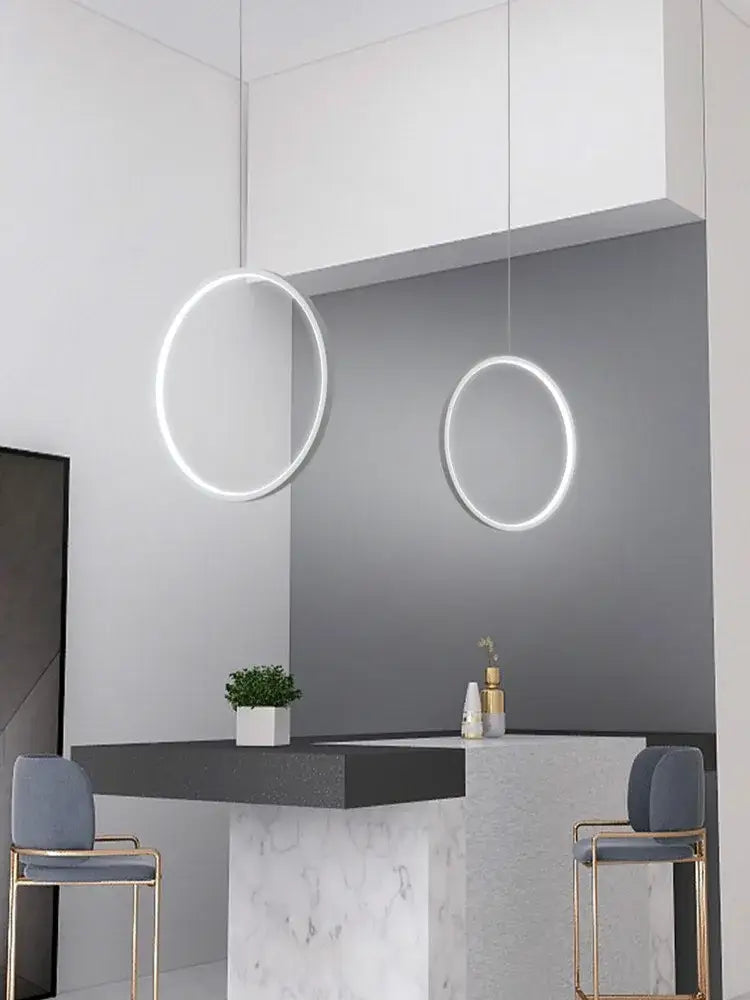 Two minimalist black circular pendant lights with glowing white led rings suspended for living room lighting