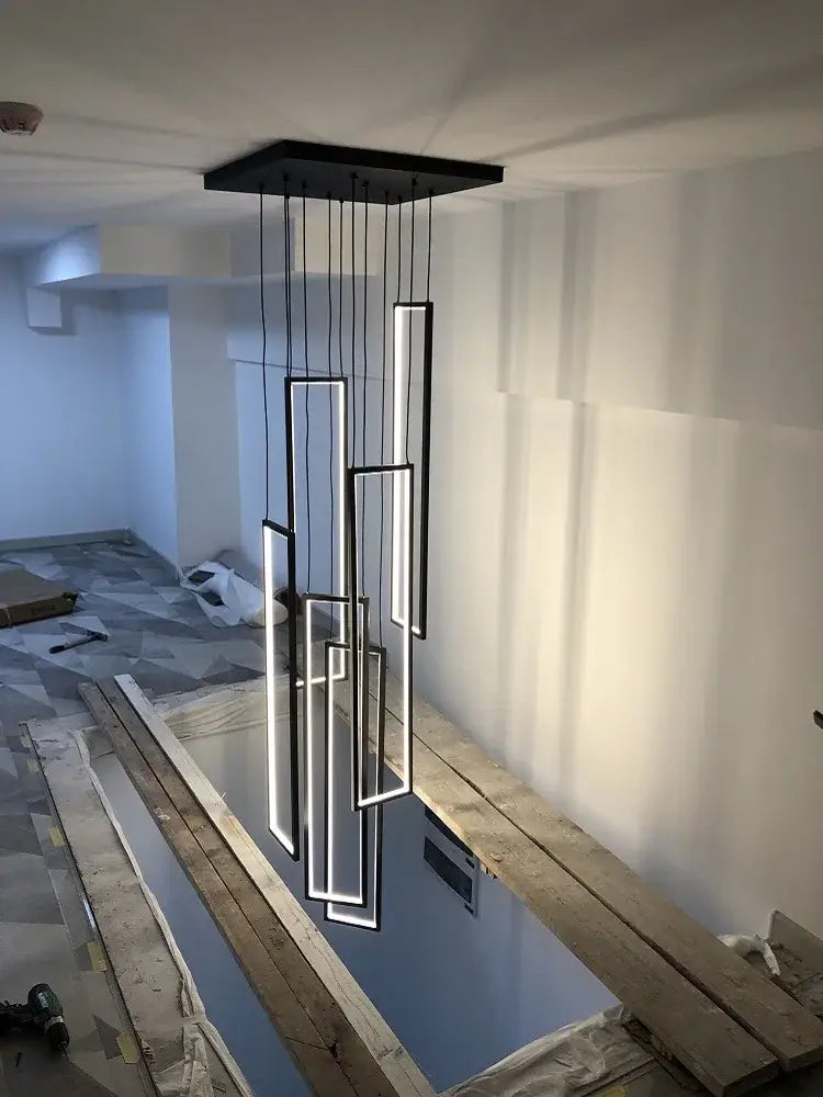 Modern black rectangular led stair chandelier with glowing white panels suspended from a square ceiling mount by decorbites led