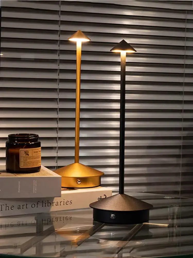 Two decorbites™ led table lamps with gold and black finishes and tapered conical tops on a glass surface