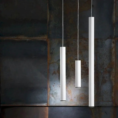 Three minimalist white cylindrical decorbites led tube pendant lights hang against a rustic metal wall for kitchen decor