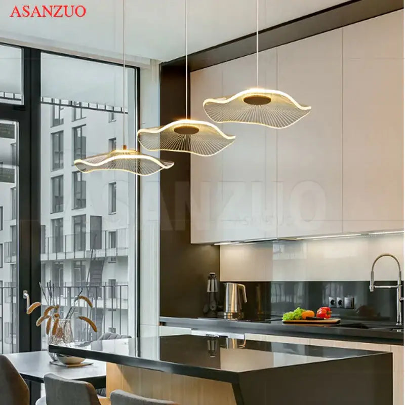Three gold-toned decorbites lotus leaf single pendant lamps with modern fan-like design hang above kitchen island