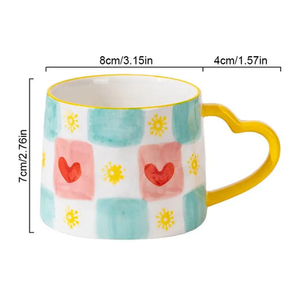 A decorbites love heart ceramic mug with a yellow heart handle and pink hearts and yellow suns on teal checkered background