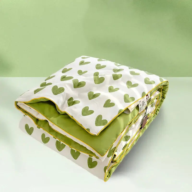 A neatly folded decorbites love print soft summer quilt with white green heart print exterior and olive green interior