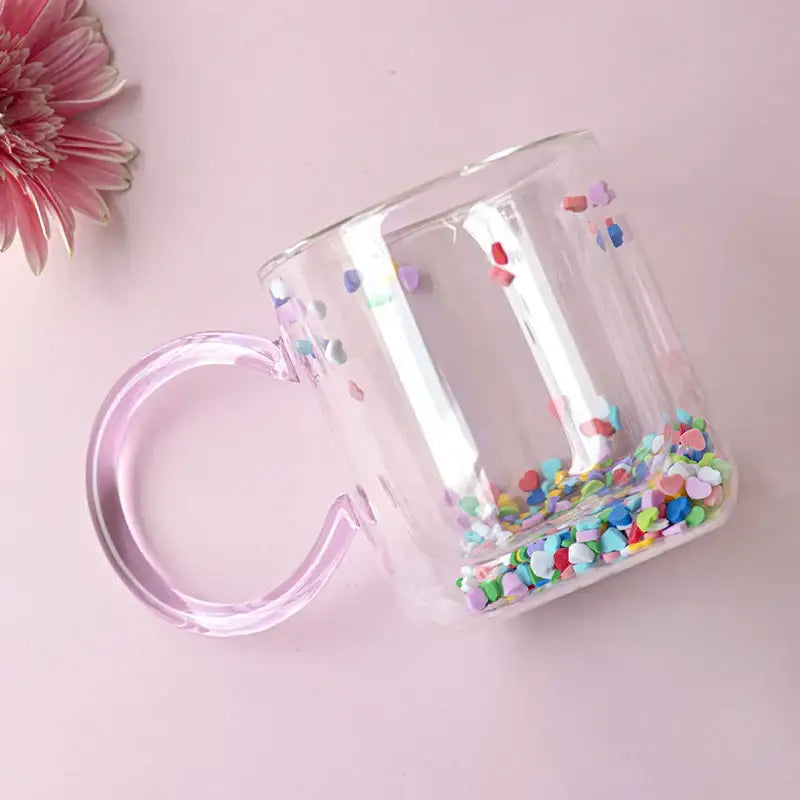Clear glass cup with translucent pink handle and colorful heart confetti in DecorBites love quicksand double bottom glass cup