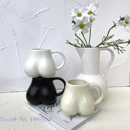 White ceramic coffee cup with playful sculpted buttocks shape and subtle speckled texture by DecorBites