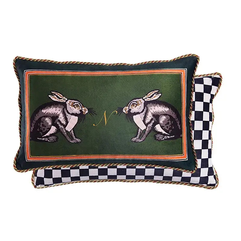 Dark green velvet decorative pillow cover with embroidered rabbits, gold monogram, orange border, and braided trim