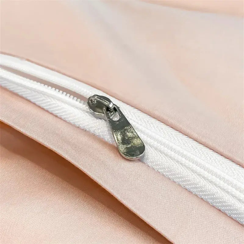 A silver-toned zipper pull on a white duvet cover zipper track against soft pink satin in DecorBites™ bedding set