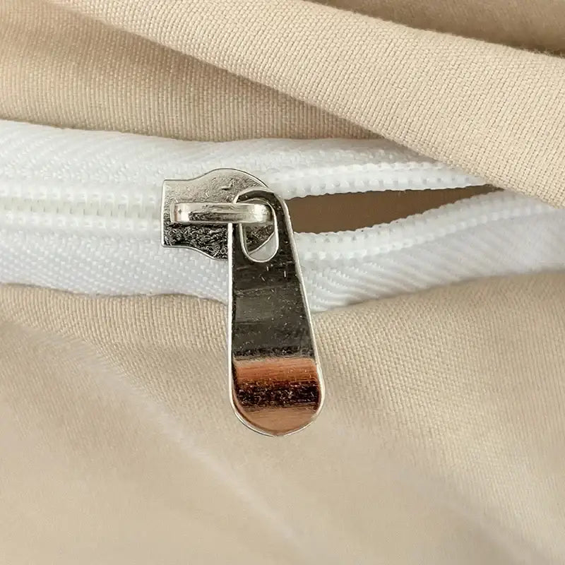 Silver zipper pull on white fabric zipper of decorbites luxurious beige cotton bedding set detail