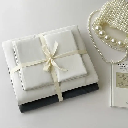 A DecorBites™ luxurious cotton bedding set featuring a white satin sheet set tied with cream ribbon and a black pillowcase