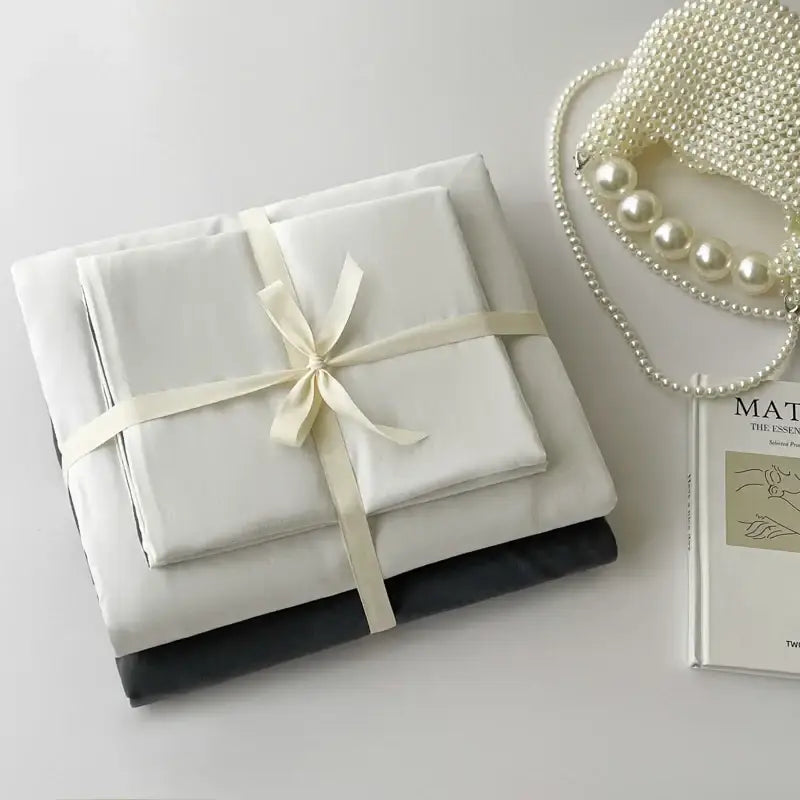A DecorBites™ luxurious cotton bedding set featuring a white satin sheet set tied with cream ribbon and a black pillowcase