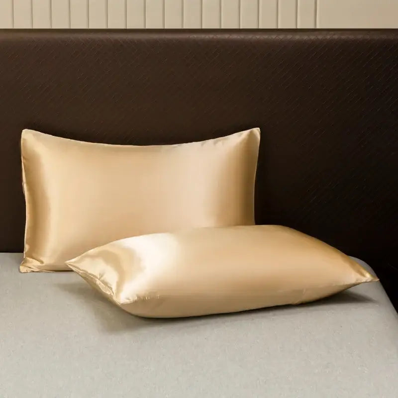 Two elegant gold satin pillowcases from decorbites™ luxurious solid color bedding set resting on a bed