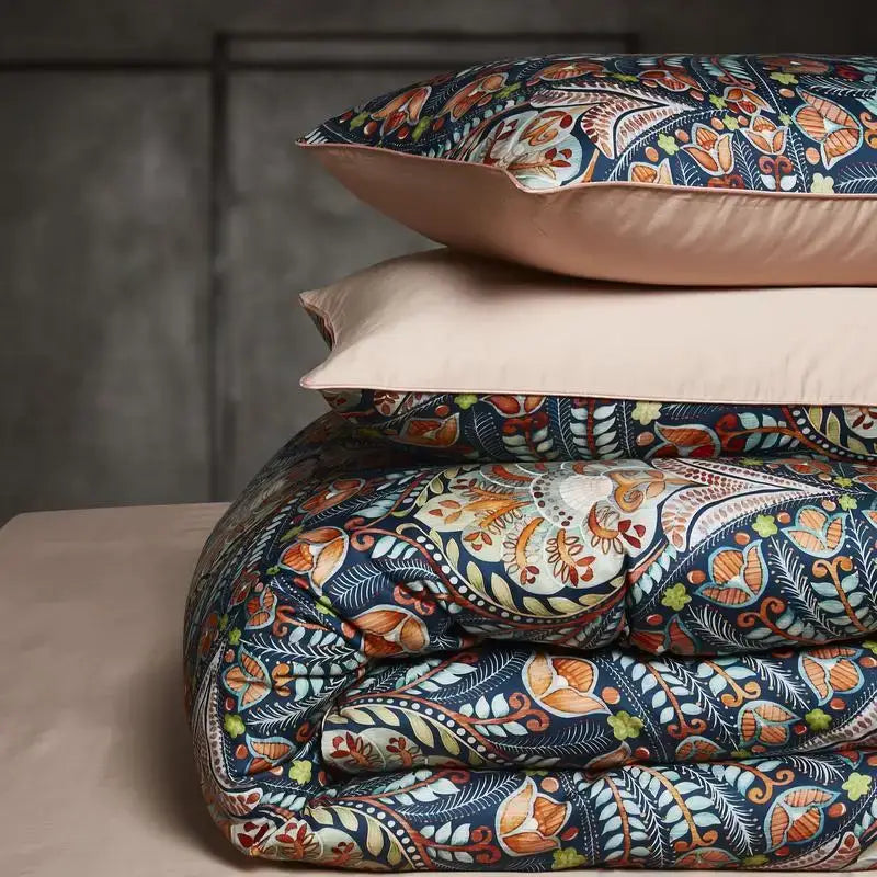 Stacked duvet cover and pillowcases set in navy blue with orange floral patterns and blush pink satin trim in egyptian cotton