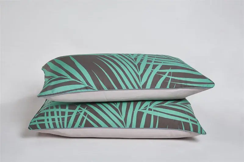 Two stacked rectangular pillowcases with bold teal and dark gray tropical leaf pattern in egyptian cotton for luxury bedding