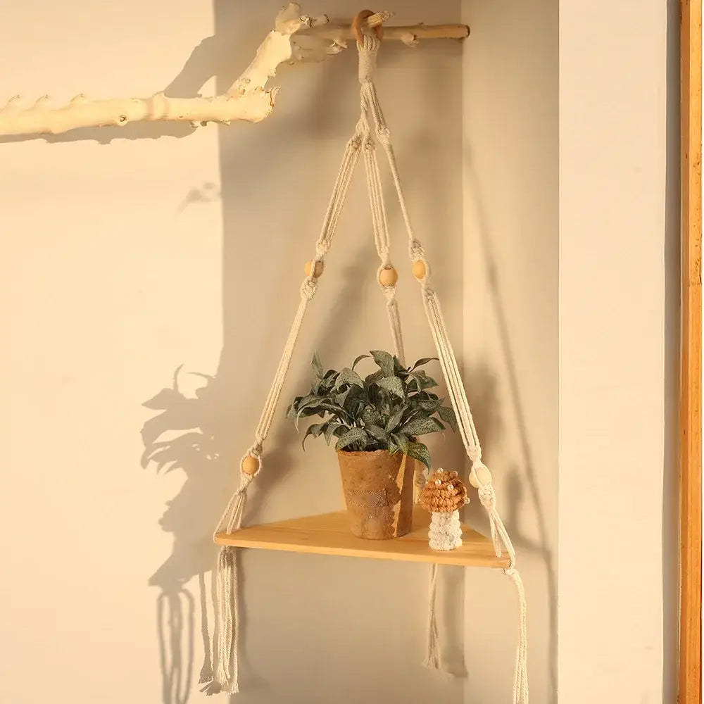 Beige macrame wall hanging corner shelf with wooden accents and a small plant for boho decor by decorbites