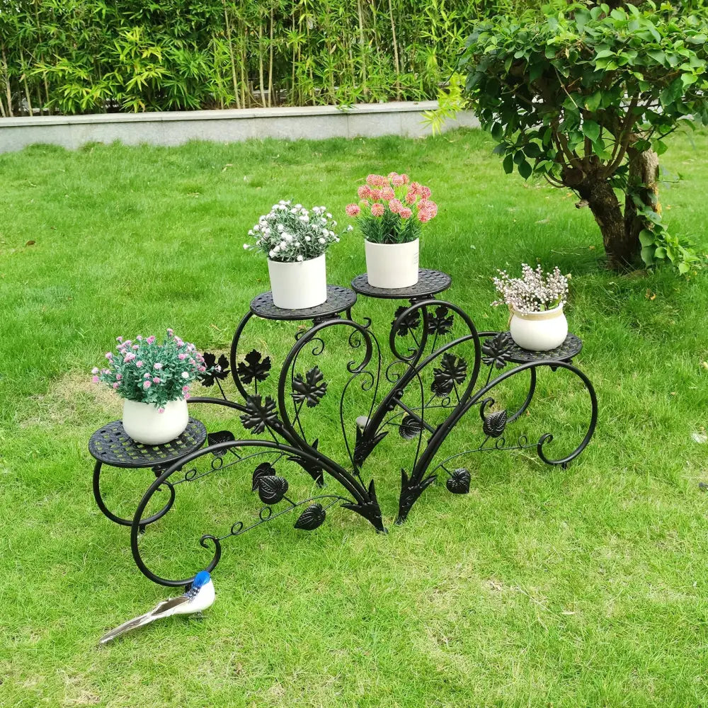 Black wrought iron metal plant stand with ornate leaf vine design and three tiers holding white ceramic pots