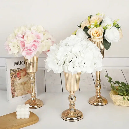 Three elegant gold-toned metal trumpet vases by DecorBites holding soft pink and white artificial flowers