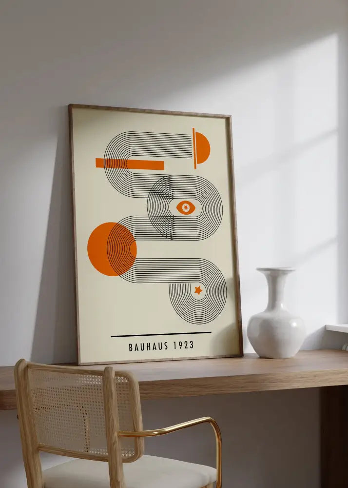 A mid century geometric canvas art with orange and black abstract design in a light wood frame by DecorBites