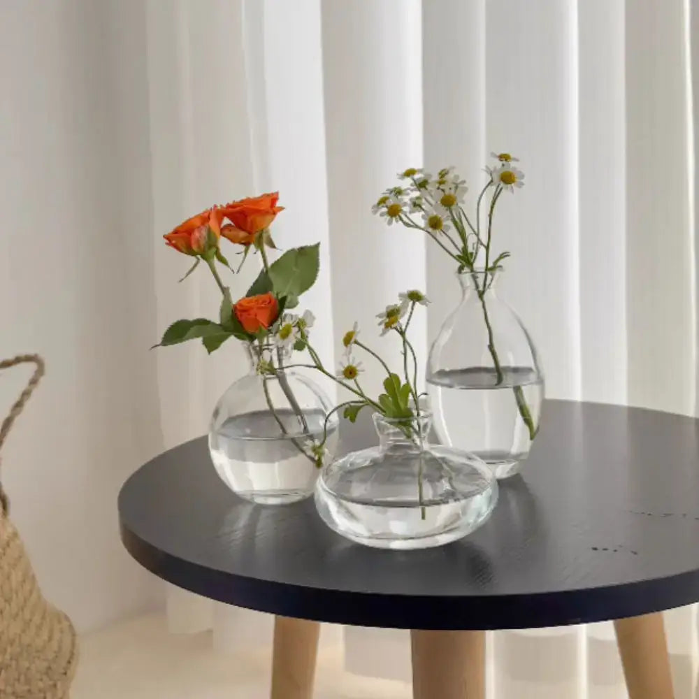 Three clear glass mini flower vases of varying shapes holding fresh flowers for home decor by decorbites