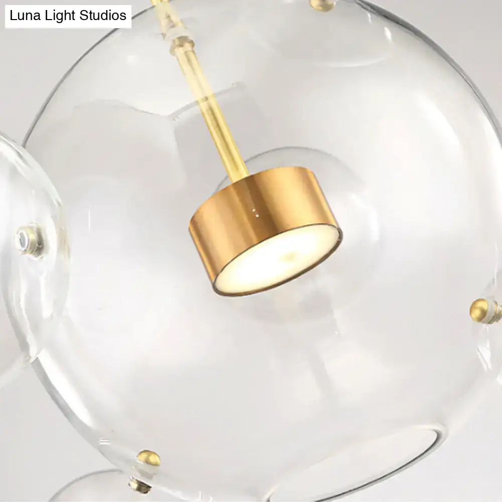 Clear glass globe pendant light with brushed gold fixture and brass bubble accents in modern design by DecorBites™