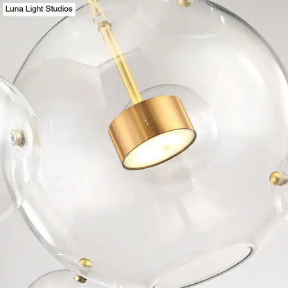 Clear glass globe pendant light with brushed gold fixture and brass bubble accents in modern design by DecorBites™