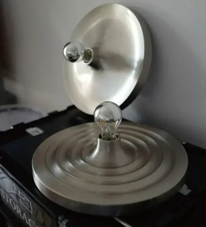 A sleek brushed metallic bauhaus lamp with circular base and two exposed glass bulbs by DecorBites Bauhaus