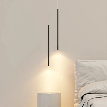 Two sleek black cylindrical decorbites™ modern 2cm led pendant lights hang over a minimalist bedside table and bed