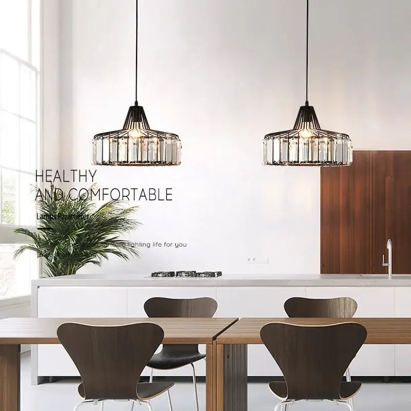 Two black-framed pendant lamps with crystal glass cylindrical accents hang above a dining table by DecorBites™ Nordic LED crystal chandelier