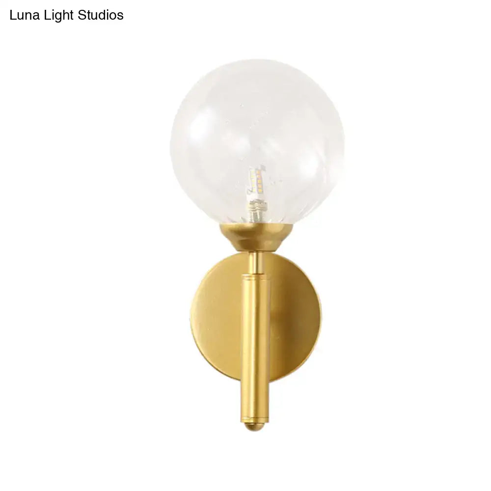 Modern brass wall lamp fixture with gold-toned base and clear spherical glass globe for bedroom lighting