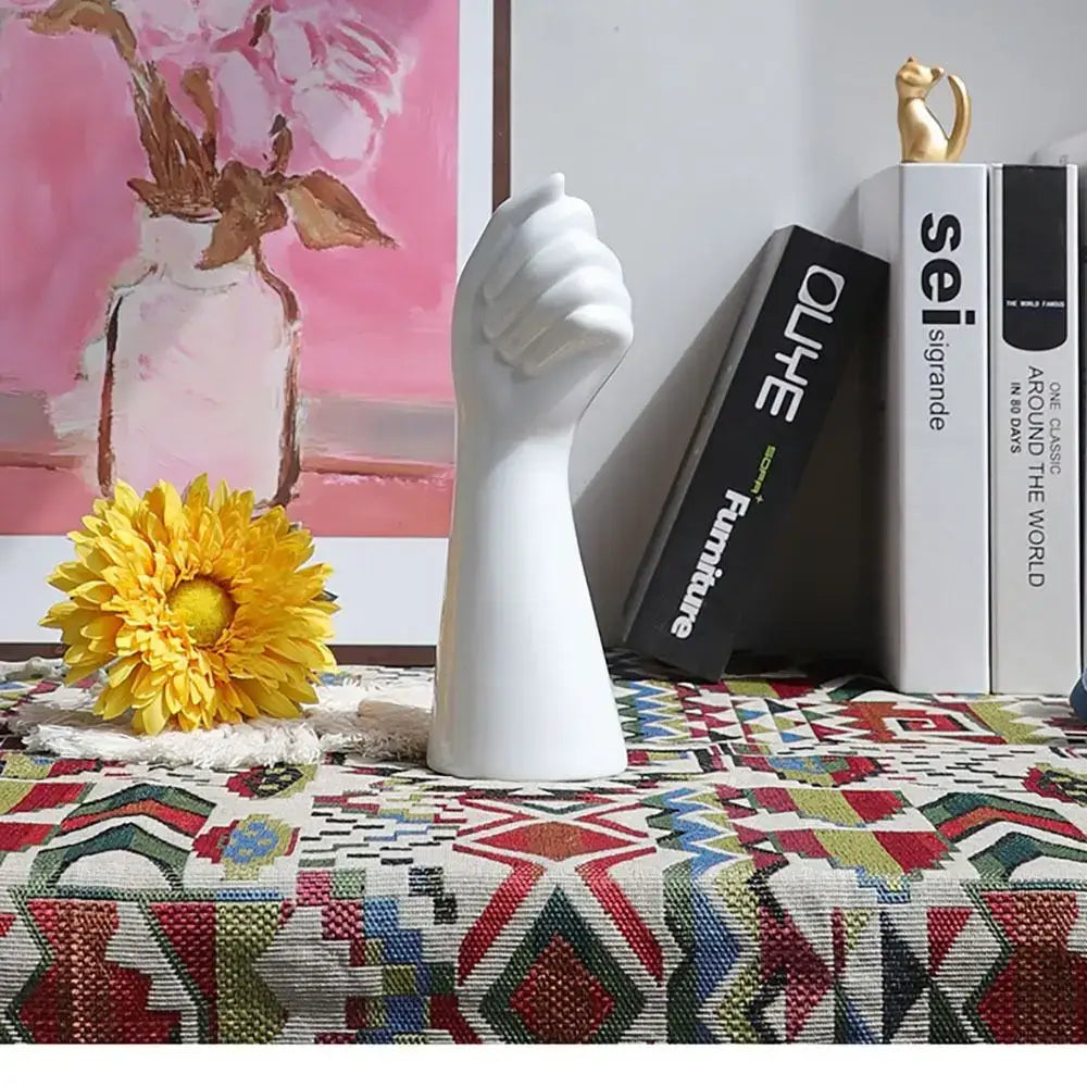White ceramic arm vase in a clenched fist design standing upright on a patterned surface by DecorBites™