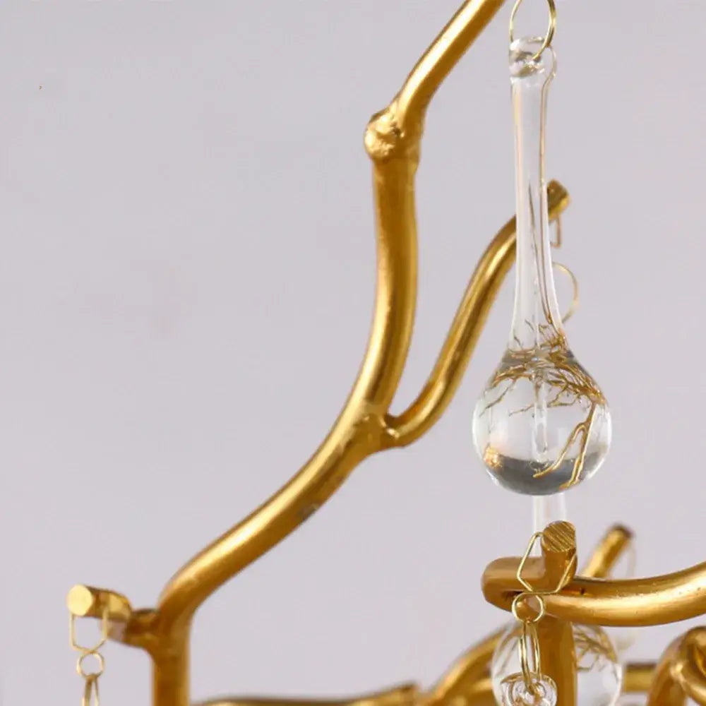 A clear glass teardrop pendant with gold wire detailing hangs from a golden branch frame in a decorbites crystal chandelier for living room