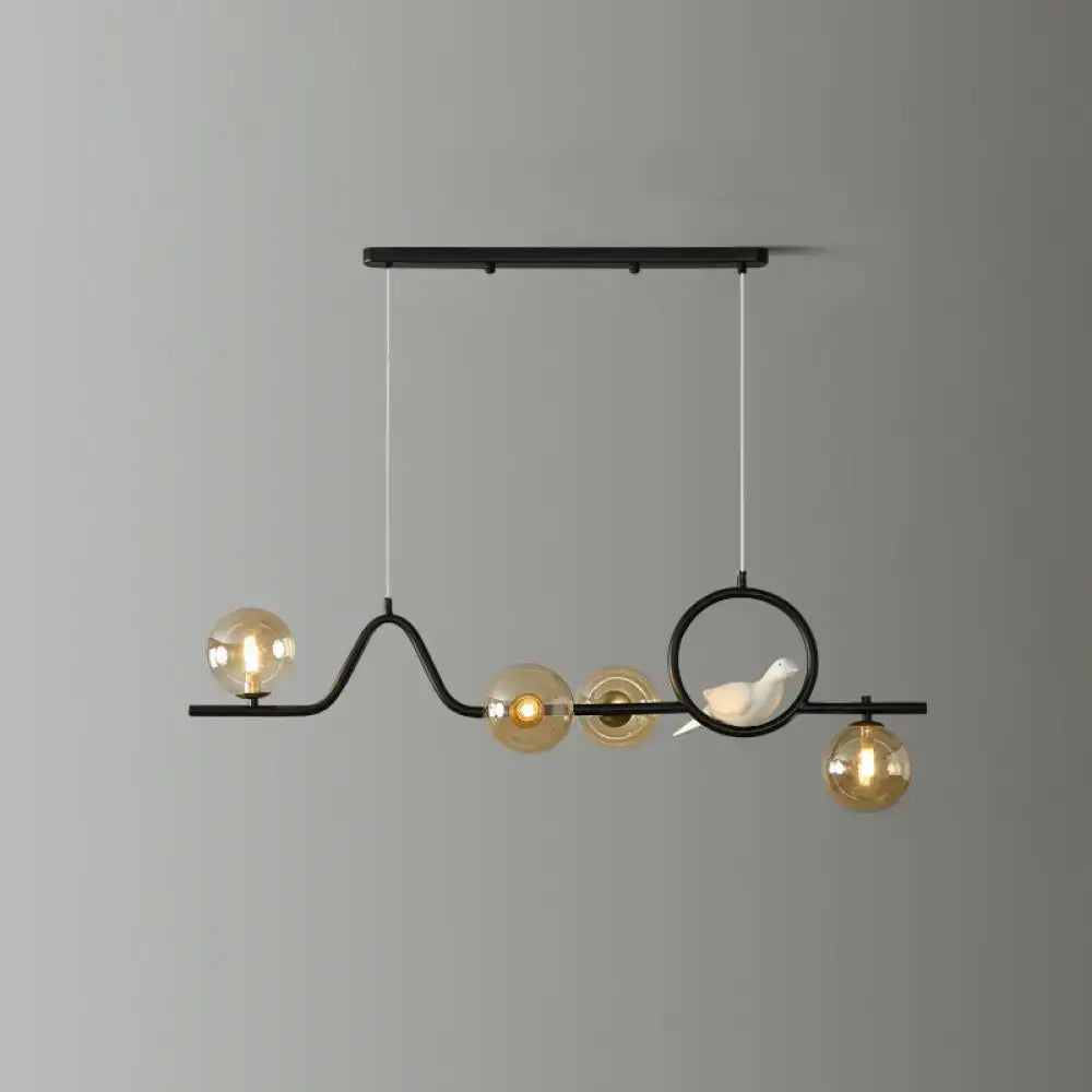 Black metal DecorBites™ curve island ceiling light with four amber glass globes and a white ceramic bird for dining room