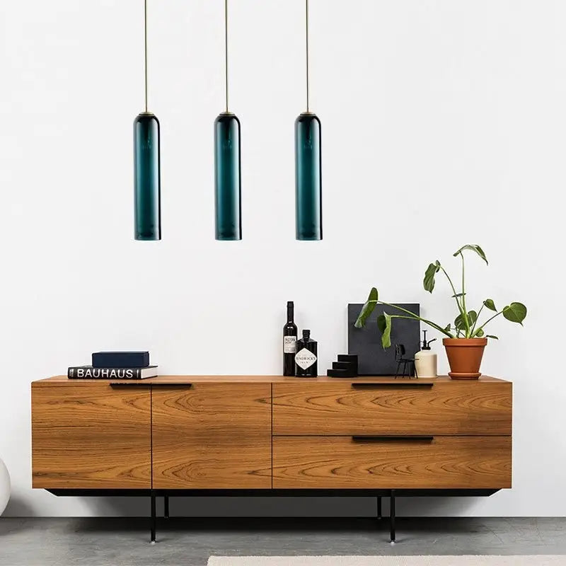 Three sleek teal glass pendant lights by DecorBites modern pendant light offer a stylish lighting solution above a wooden table
