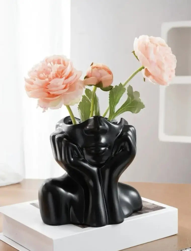 Black glossy resin vase from decorbites shaped like a woman’s head with hands framing face holding pink peonies body shaping human body