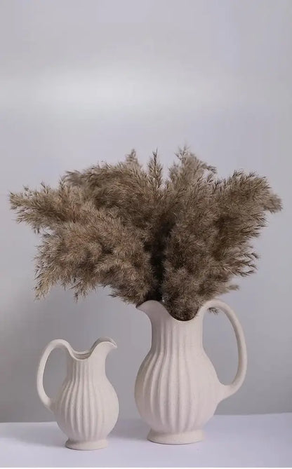 Cream-colored ins style ceramic spiral vase with vertical ribbed texture and curved handle filled with dried pampas grass