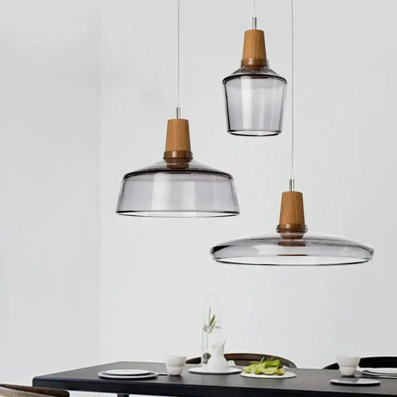 Three decorbites™ modern nordic glass light fixtures with smoked glass shades and warm wood accents hang above dining table