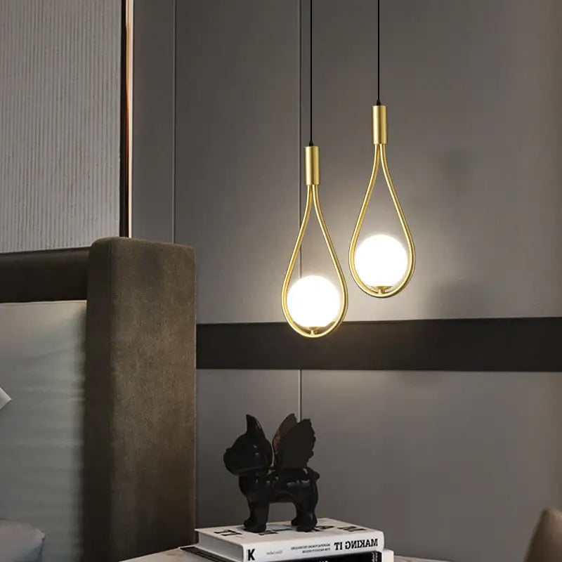 Two elegant gold-toned decorbites™ modern nordic pendant lights with teardrop frames and glowing bulbs hanging from black cords