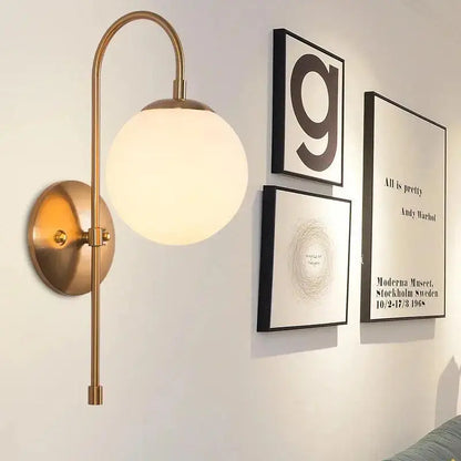 Brass-finished DecorBites modern Nordic wall lamp by Olsson with curved arm and frosted glass globe shade
