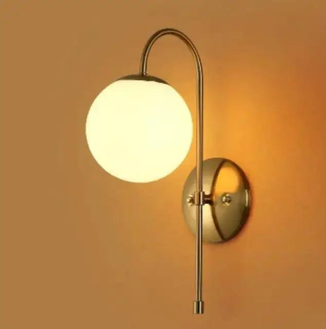A sleek brass-finished olsson wall lamp with a curved arm and glowing spherical glass shade from decorbites modern nordic series