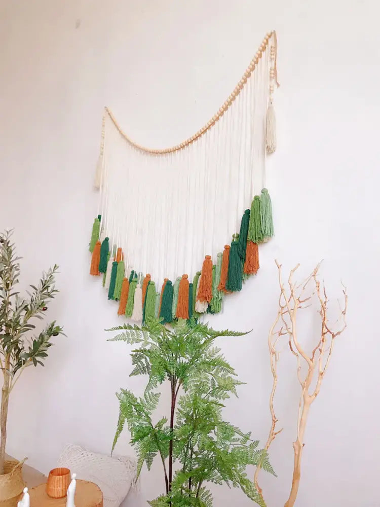 A moroccan bohemian wall decor tapestry featuring a curved wooden bead arch with white green and orange tassels
