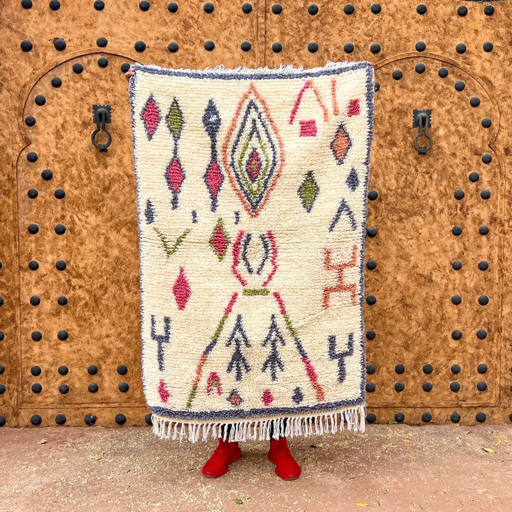 Cream-colored moroccan handmade azilal carpet with intricate red green navy geometric patterns and fringed edges by skilled artisans