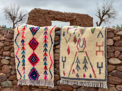 Two moroccan handmade azilal rugs with vibrant geometric patterns in pink blue purple and green on cream background by skilled artisans